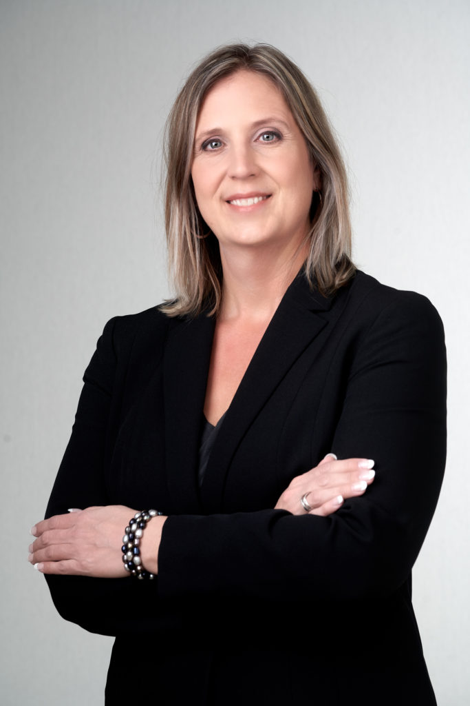 Maureen Terra posing for a professional portrait, in front of a grey and white gradient background. 